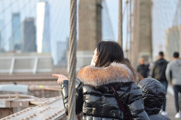 young  woman walking in the city nyc on the brooklynbridge pointing at different sights or points of interest