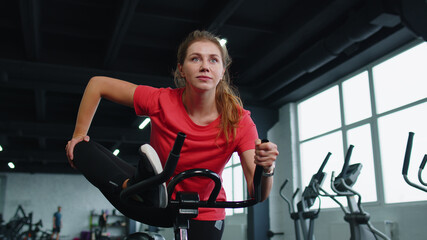 Fototapeta na wymiar Group of athletic young girls training stretching on spin stationary bike riding in gym. Fit women performs aerobic training workout cardio routine on simulators cycle training on exercise bike indoor