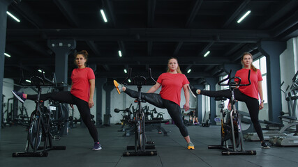 Class group of young women exercising stretching on stationary cycle machine bike in gym. Modern sport activity, workout, healthy lifestyle. Athletic female girls spin bike, indoors. Slow motion