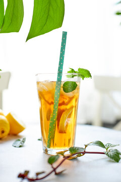 Iced iced tea in a glass with a straw, mint leaf and lemon slices inside. Cool drinks in the heat. Vertically photo