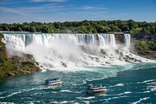 Two tours boats on the Niagara River pass in front of the American Falls in Niagara Falls New York. The photo was taken from Niagara Falls Ontario Canada.
