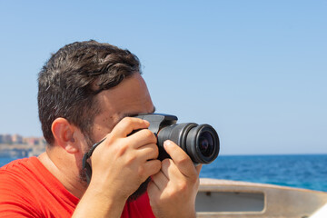Fototapeta na wymiar male photographer taking pictures with professional camera on summer next by the sea. Tourist taking photos of the beautiful landscape view on a ship riding