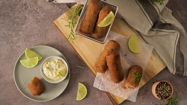 Meat croquets with rosemary leaves and lemons on wooden cutting board in a kitchen counter top.
