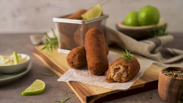 Meat croquets with rosemary leaves and lemons on wooden cutting board in a kitchen counter top.
