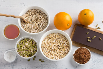 Ingredients for cooking chocolate sausage with oatmeal and seeds: oatmeal, oranges, seeds, cocoa, honey, chocolate and spices on a light blue background. Homemade healthy food preparation