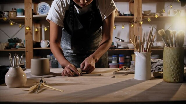 Young woman potter cutting a piece of clay for a handle