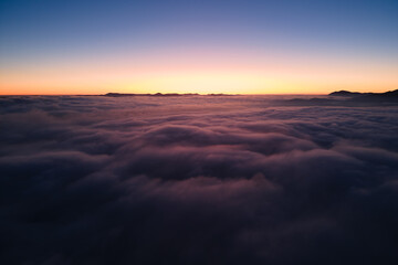 Fototapeta na wymiar Aerial view of colorful sunrise over white dense fog with distant dark silhouettes of mountain hills on horizon