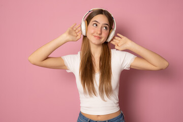 Obraz na płótnie Canvas Young smiling woman wearing headphones listening music over pink background.