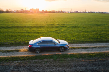 Fototapeta premium Aerial view of sedan car driving fast on dirt road at sunset. Traveling by vehicle concept