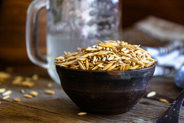 On the wooden kitchen table are a ceramic bowl of oat grains, a glass cup with oat kvass on a...