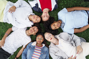 Relaxed teenager friends lying together on green grass with eyes closed, dreaming and sleeping