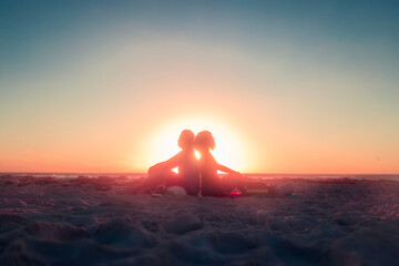 Pareja de enamorados sentados de espaldas en la playa a contraluz al amanecer