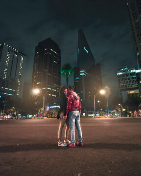 Pareja de j&oacute;venes enamorados tomados de las manos frente a las luces nocturnas de la ciudad