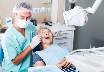 Male dentist treating mature female patient in dental office