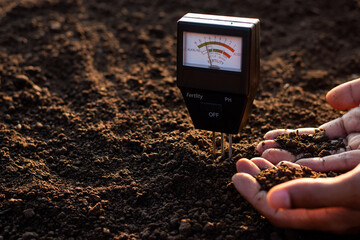 A soil meter and a farmer's hands are picking up soil for planting.