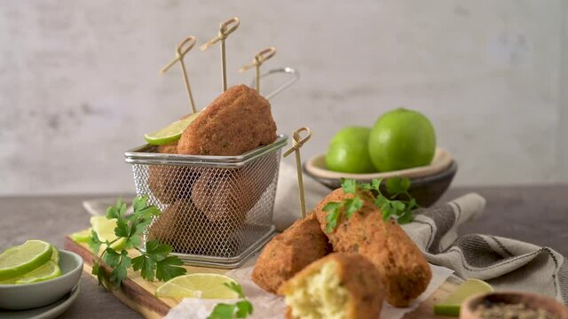 Meat croquets with rosemary leaves and lemons on wooden cutting board in a kitchen counter top.