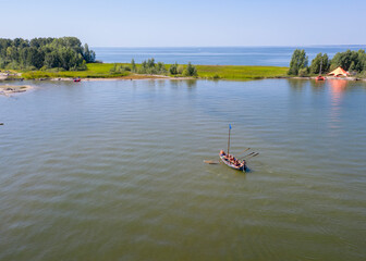 Aerial view of a wooden boat with oars approaches the island in summer