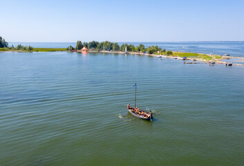 Aerial view of a wooden boat with oars approaches the island in summer