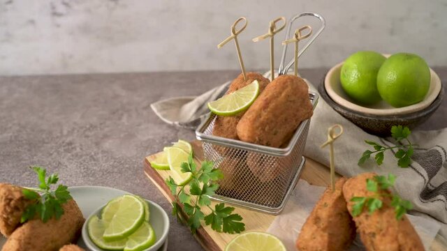 Meat croquets with rosemary leaves and lemons on wooden cutting board in a kitchen counter top.