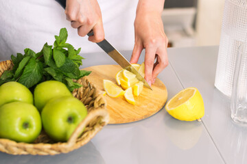 Woman making detox drink with lemon and mint in the kitchen at home. Rejuvenating invigorating water lemon, antioxidant.
