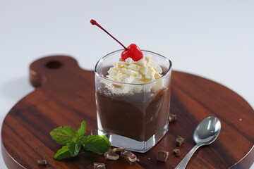 Glass jar with chocolate pudding with topped cherry creamy on a wooden board