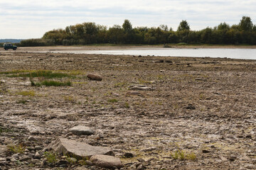 Drying bottom of the river against the background of a natural landscape - shore, trees, sky. Low water level in the reservoir.