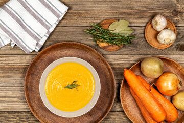 Carrot and potato soup bowl on a drift wood table with vegetables in a wood plate, napkin, garlic,...
