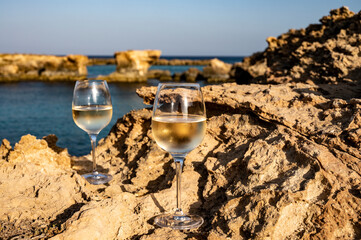 Two glasses of cold white dry white wine served on rocks in blue sea bay near Protaras touristic town on Cyprus