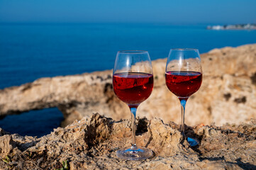 Two glasses of rose dry white wine served on rocks in blue sea bay with Love Bridge on background near Ayia Napa touristic town on Cyprus