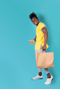 happy and handsome afro young man standing in front of a blue studio background with a shopping bag. High quality photo