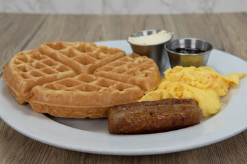 Round waffle for tradional breakfast with sausage, eggs, syrup, and butter to fill the appetite