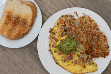 Overhead view of eggs scrambled in a hearty omelette served with hash browns and toast for a tradional breakfast