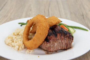 Thick cut of steak seasoned and cooked to perfection with onion rings, rice, and string beans on the dinner plate