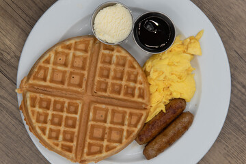 Overhead view of round waffle for tradional breakfast with sausage, eggs, syrup, and butter to fill the appetite