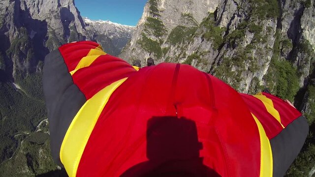 First-person perspective from a wingsuit flyer soaring by mountains