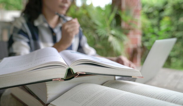 Books on table with woman and computer laptop at the background. Home setting.