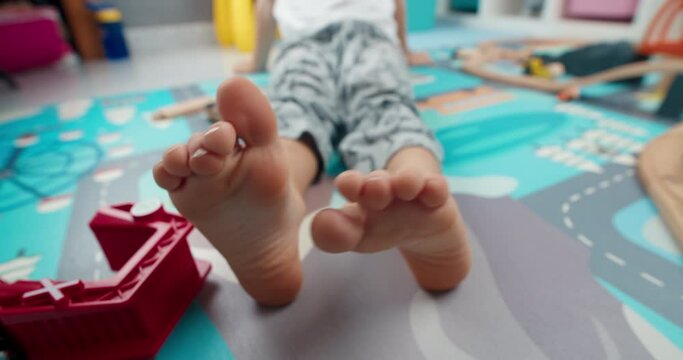 Closeup of cute child foot moving fingers laying on the floor in home barefoot. Carefree childhood enjoying in kid room after playing with toys
