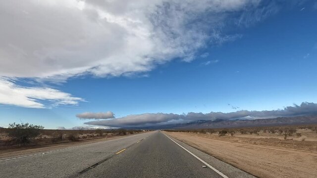 Driving through the Mojave Desert with arid landscape on both sides of the car and scenic mountains ahead - driver point of view hyper lapse