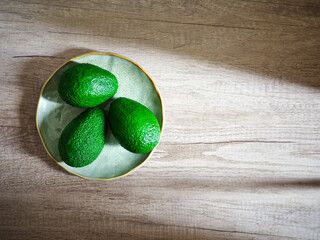 three avocados on plate on wooden surface