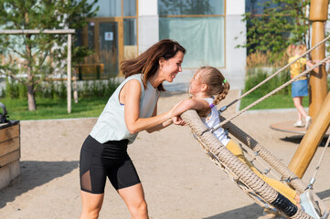 Mom and daughter swing on a round swing. Caucasian woman and little girl have fun on the playground.