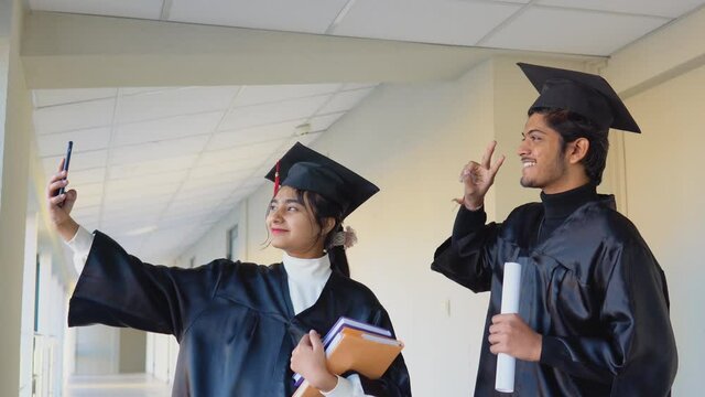 Two Indian graduates stand in a university hallway and take a selfie. Education concept