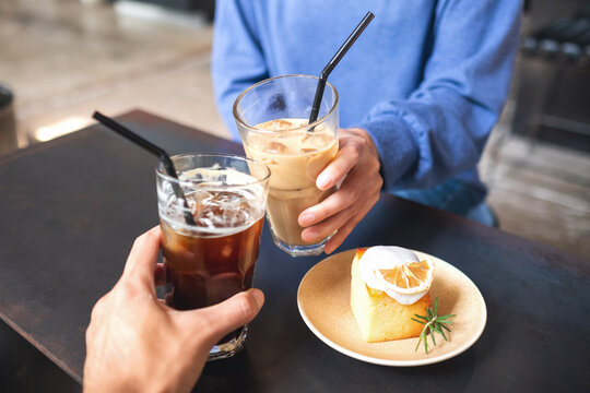 Closeup image of a couple people clinking coffee glasses together with lemon cake on the table in cafe