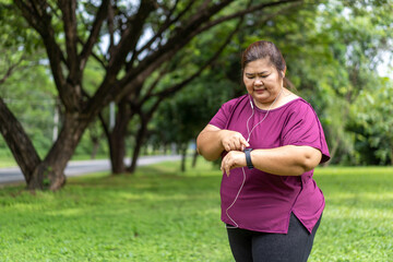 Fat woman asian checking time or heart rate from smart watch. Exercise outdoors for weight loss idea concept