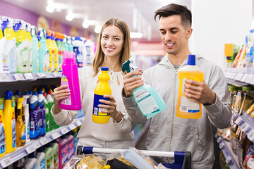 Young happy couple making purchases together, buying household chemicals in supermarket. Focus on man