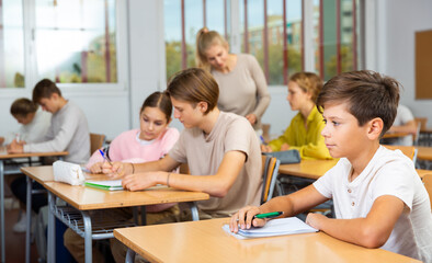 Portrait of diligent schoolboy who writing exercises at lesson in secondary school