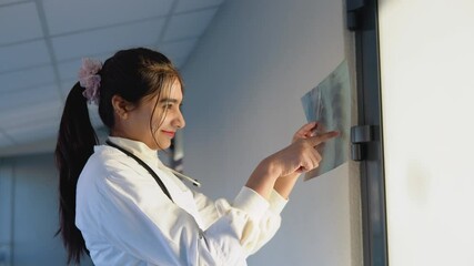 Female indian doctor or intern examines x-ray of lungs, holding it in hands indoors. Specialist holds transparent image of chest in arms, and carefully researches it