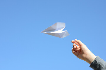 青空に紙飛行機を飛ばす子供の手