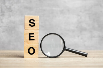 SEO (Search Engine Optimization) text wooden cube blocks and hand holding magnifying glass on table. Idea, Strategy, advertising, marketing, Keyword and Content concept
