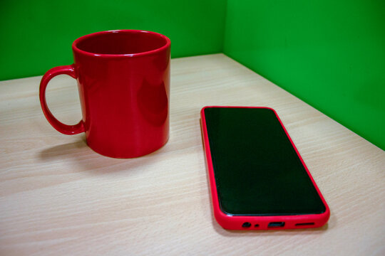 mug rojo en oficina con celular y aud&iacute;fonos