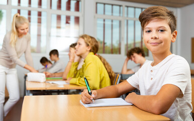 Fototapeta premium Portrait of positive schoolboy posing in classroom during lesson in secondary school